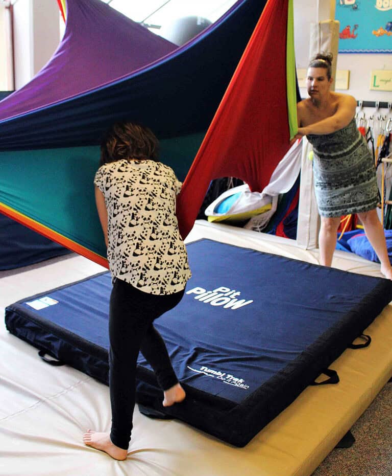 A photo of a client at a pediatric OT clinic, playing with a sensory swing with a Pit Pillow below.