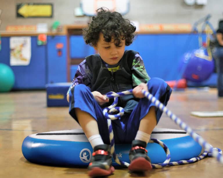 A photo of a client sitting on a Hot Spot being pulled by a pediatric OT.