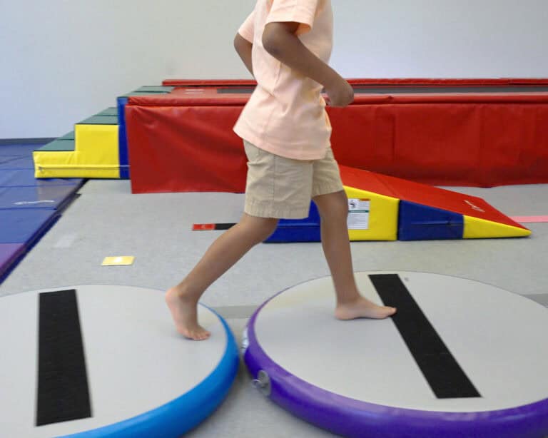 A photo of a boy at a pediatric OT clinic walking across two Hot Spots.