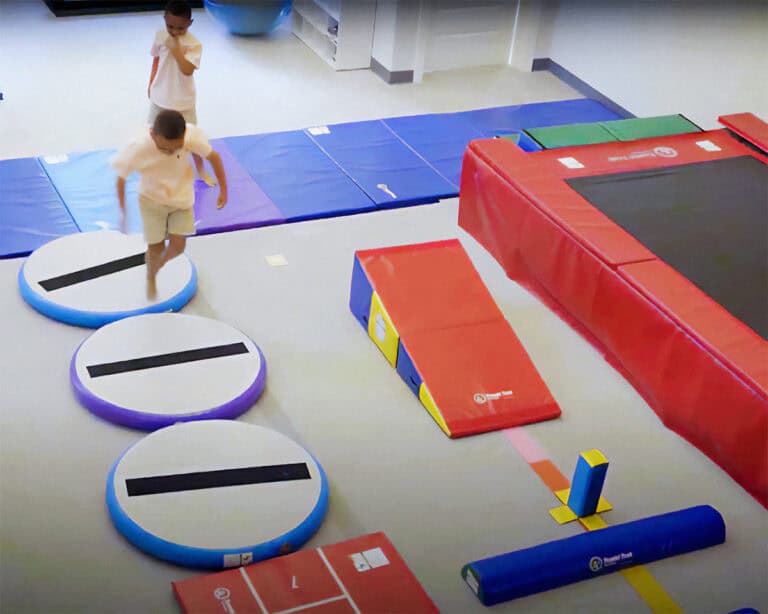 A photo from a high angle at an OT clinic showing a boy walking across several Hot Spots surrounded by other therapy equipment.