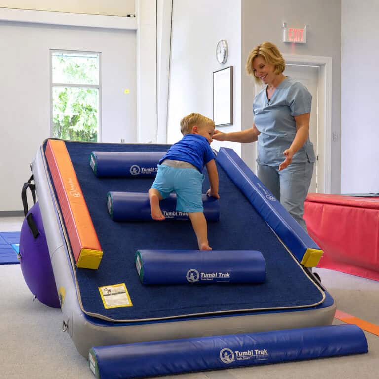 A photo of a client in an OT clinic with a pediatric OT. He is climbing a Carpet Wall with Half Rounds that is attached to an inclined Power Launch.