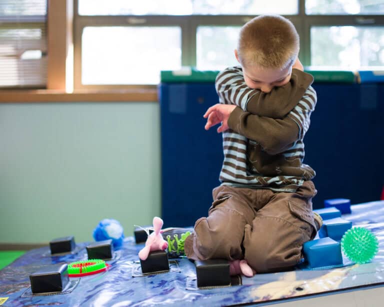 A photo of a boy being emotionally soothed while kneeling on a Climbing Wall Overlay surrounded by manipulatives.
