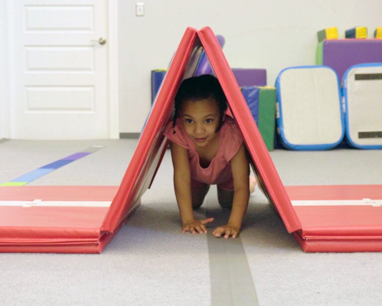A photo of a girl crawling through a tunnel made by folding the center panels of the Hopscotch Mat into an inverted V-shape.