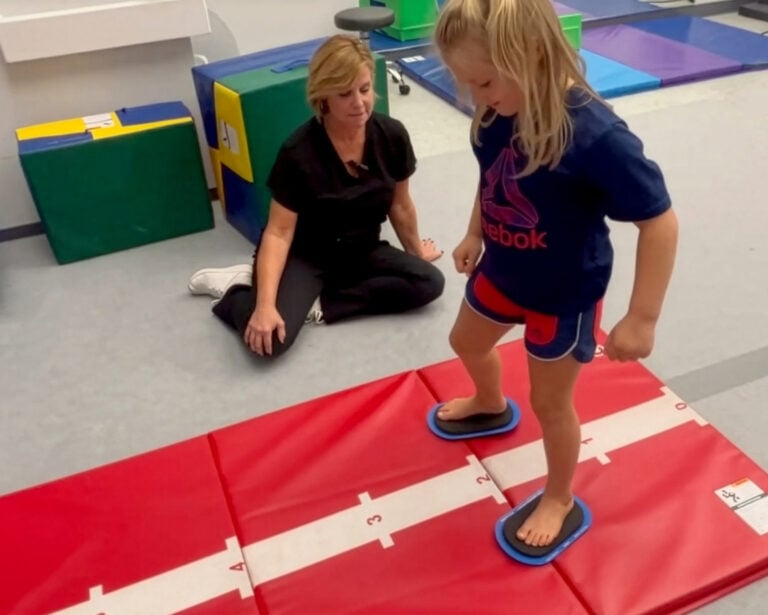 A photo showing a girl using small Sliders on a Hopscotch Mat, encouraged by her occupational therapist.