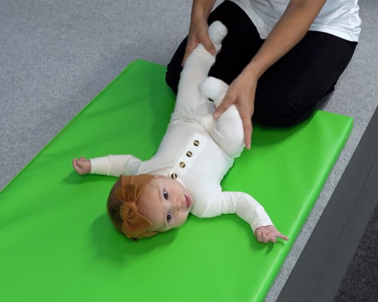 A toddler lays back on a Build-a-Mat, while her pediatric OT does range-of-motion work.