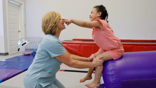 A photo of Sheri Ireland-Berk working with a client in a pediatric therapy room with PT equipment